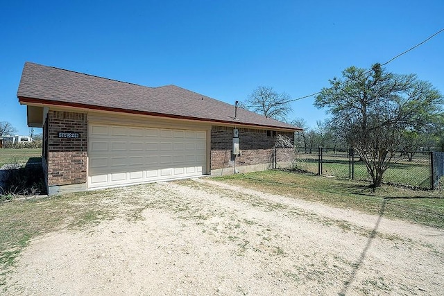 view of property exterior with brick siding, an attached garage, driveway, and fence