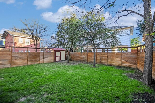 view of yard with a fenced backyard, a storage unit, and an outbuilding