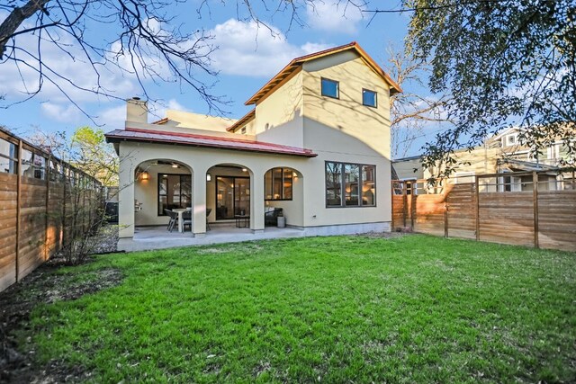 rear view of property featuring stucco siding, a fenced backyard, a chimney, a lawn, and a patio