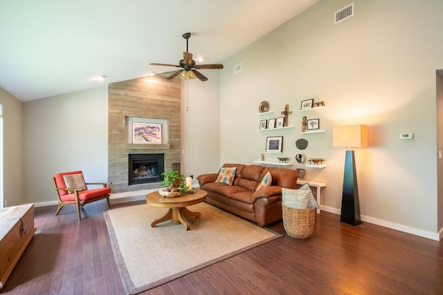 living area with a ceiling fan, dark wood-style floors, a tiled fireplace, baseboards, and high vaulted ceiling