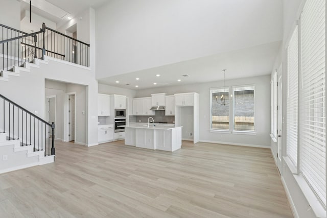 unfurnished living room featuring a chandelier, light wood finished floors, a sink, and stairway
