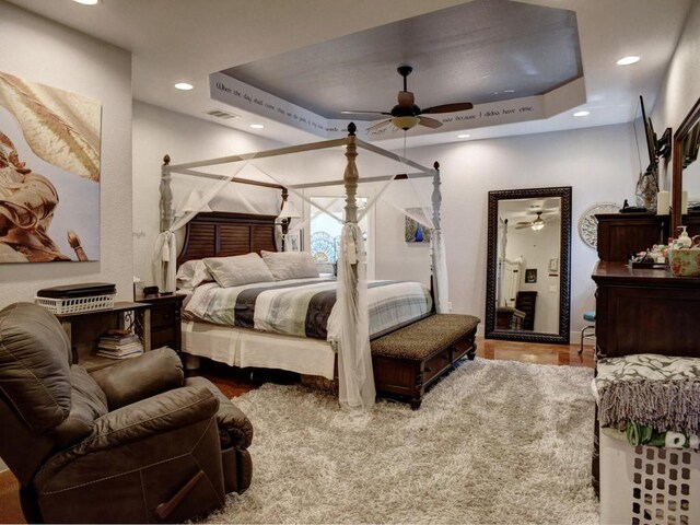 bedroom with a tray ceiling, recessed lighting, wood finished floors, and visible vents