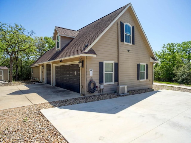 view of side of home with concrete driveway, roof with shingles, central air condition unit, an attached garage, and a storage unit