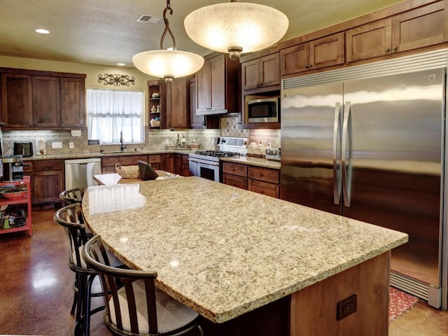 kitchen with visible vents, a kitchen island, a sink, high quality appliances, and decorative backsplash