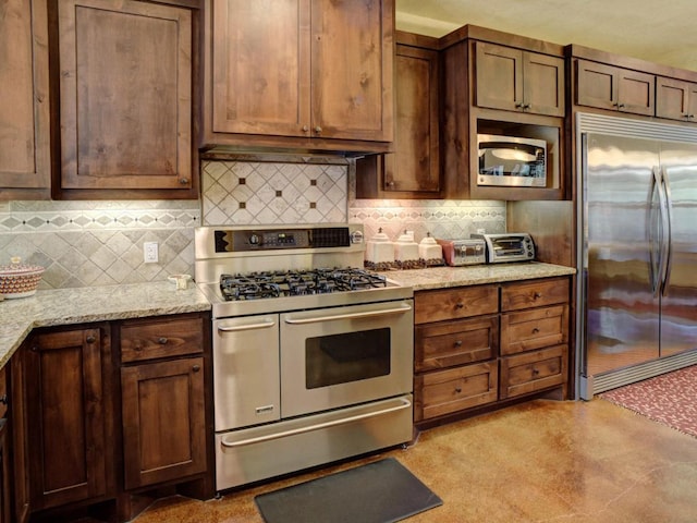 kitchen featuring under cabinet range hood, built in appliances, light stone counters, and decorative backsplash