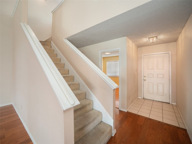 foyer entrance featuring baseboards, stairway, wood finished floors, and a textured ceiling