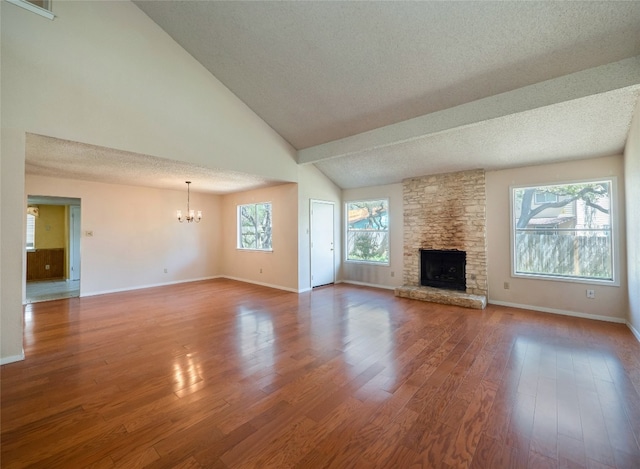 unfurnished living room with a stone fireplace, baseboards, a chandelier, a textured ceiling, and wood finished floors