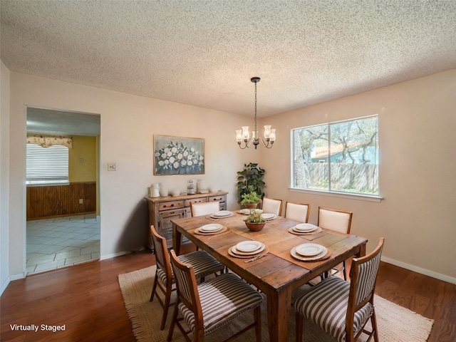 dining area featuring a textured ceiling, wood finished floors, a notable chandelier, and baseboards