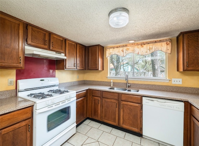 kitchen with a sink, white appliances, a textured ceiling, brown cabinets, and under cabinet range hood