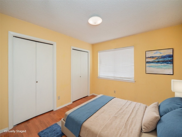 bedroom featuring baseboards, two closets, and wood finished floors