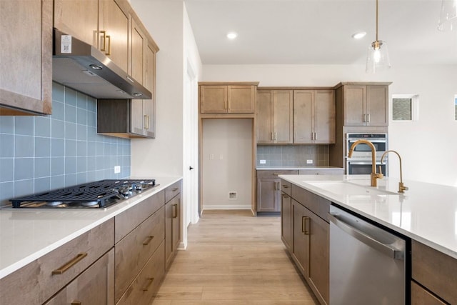 kitchen with under cabinet range hood, light countertops, light wood-style floors, decorative backsplash, and appliances with stainless steel finishes