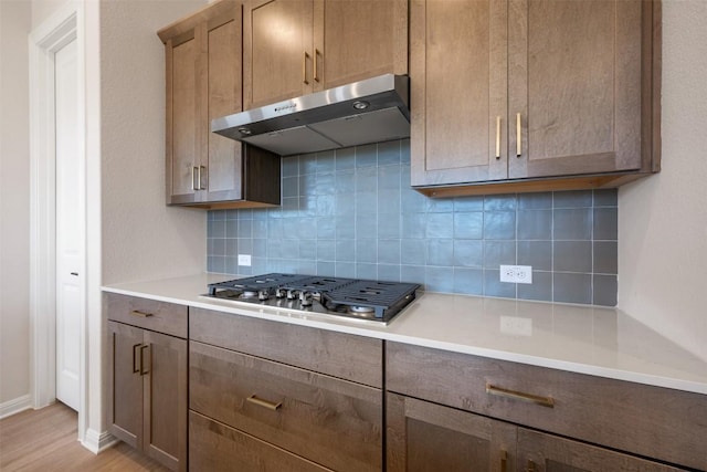 kitchen featuring light countertops, stainless steel gas cooktop, under cabinet range hood, and tasteful backsplash
