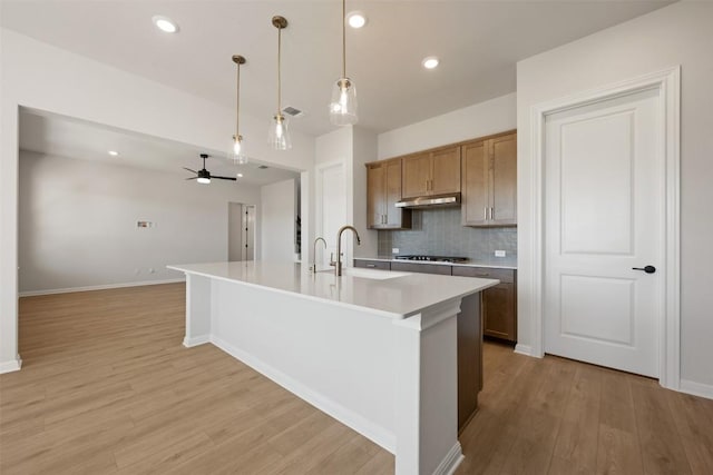 kitchen featuring backsplash, light countertops, a sink, a center island with sink, and light wood-style flooring