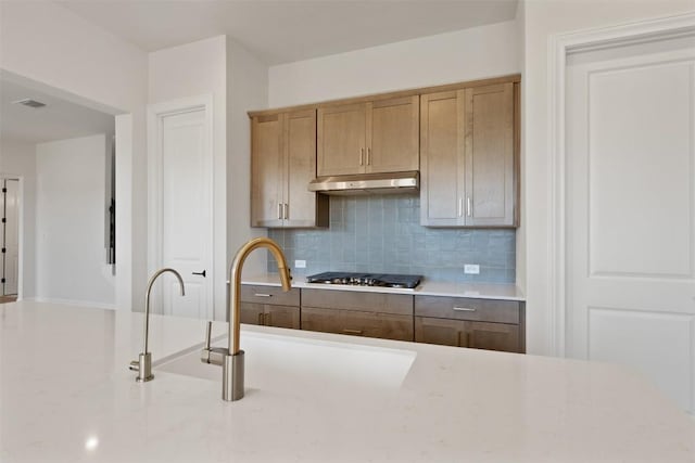 kitchen featuring stainless steel gas cooktop, a sink, tasteful backsplash, visible vents, and under cabinet range hood