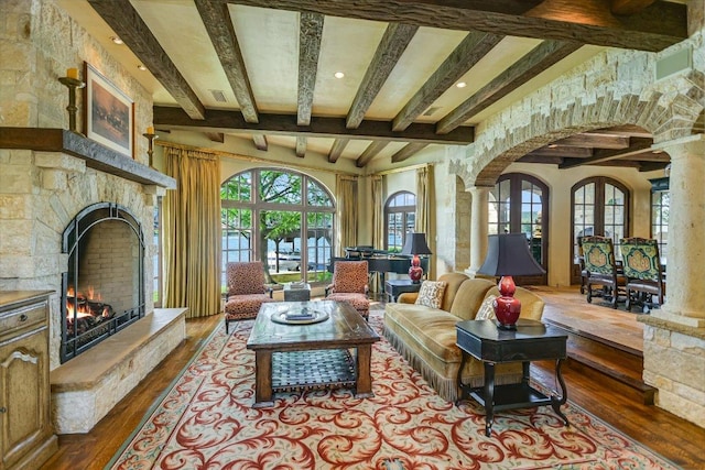 6704 Pixie Cv, Austin, TX 78746 - living area with hardwood / wood-style flooring, beamed ceiling, arched walkways, decorative columns, and a warm lit fireplace