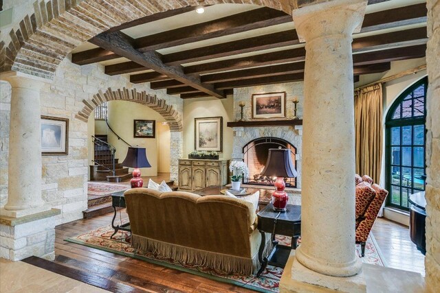 6704 Pixie Cv, Austin, TX 78746 - living room featuring ornate columns, beamed ceiling, wood-type flooring, a stone fireplace, and arched walkways