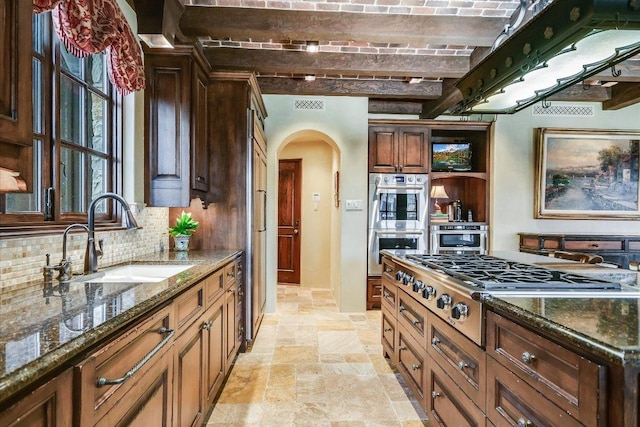 6704 Pixie Cv, Austin, TX 78746 - kitchen with arched walkways, stainless steel appliances, stone tile floors, dark stone countertops, and decorative backsplash