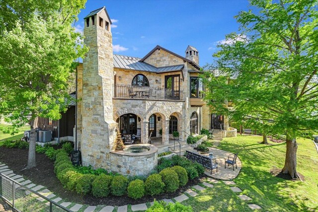 6704 Pixie Cv, Austin, TX 78746 - back of property with a balcony, a chimney, a standing seam roof, stone siding, and a patio