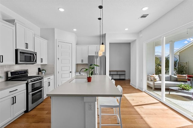 130 Volterra Ln, Dripping Springs, TX 78620 - kitchen with appliances with stainless steel finishes, backsplash, hanging light fixtures, a center island with sink, and white cabinets