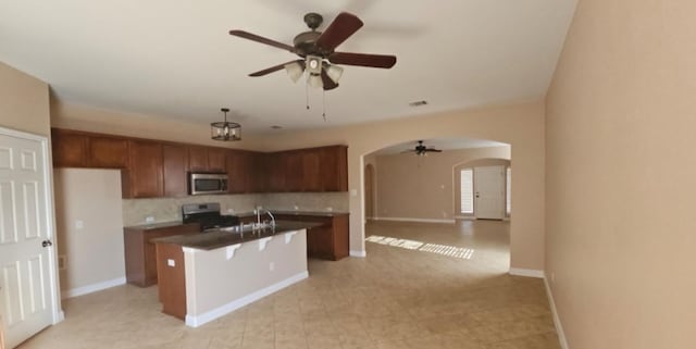19500 Moorlynch Ave, Pflugerville, TX 78660 - kitchen featuring stainless steel microwave, stove, arched walkways, ceiling fan, and decorative backsplash