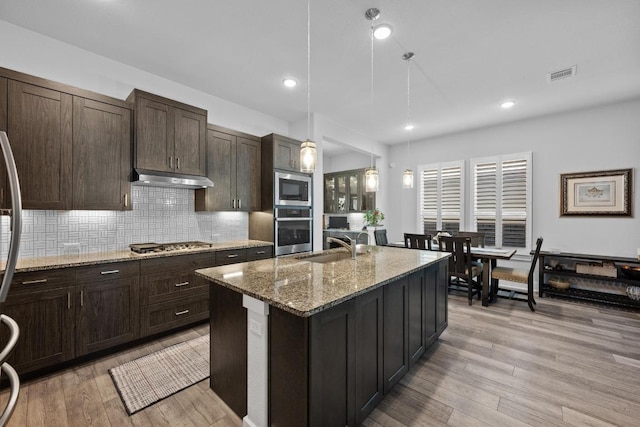 217 Palio Pl, Georgetown, TX 78628 - kitchen featuring appliances with stainless steel finishes, light wood-style flooring, decorative backsplash, light stone counters, and recessed lighting