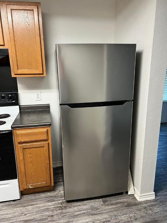 13217 Perconte Dr, Del Valle, TX 78617 - kitchen with freestanding refrigerator, white electric stove, wood finished floors, dark countertops, and a textured wall