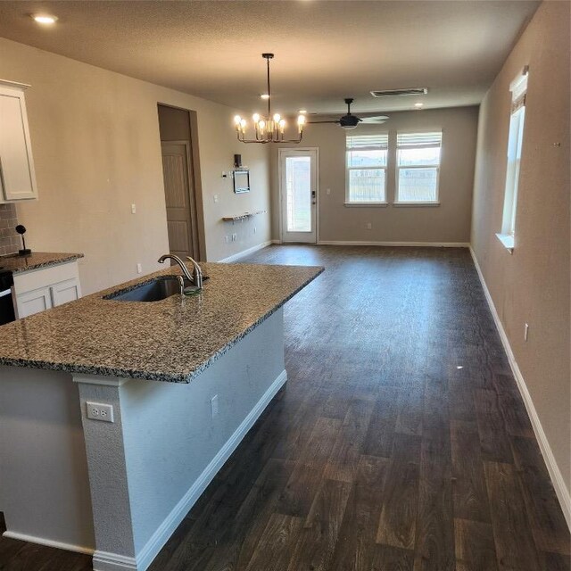 kitchen featuring baseboards, dark stone countertops, white cabinetry, and a sink