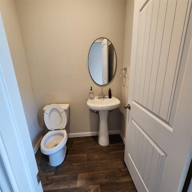 half bathroom featuring baseboards, wood finished floors, toilet, and a sink