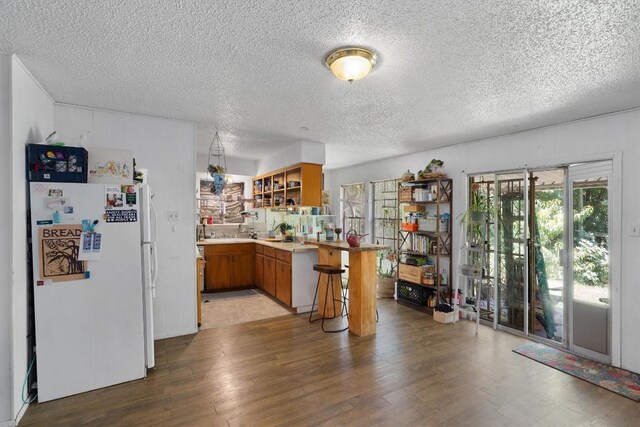 1905 Chestnut Ave, Austin, TX 78722 - kitchen featuring freestanding refrigerator, brown cabinetry, light wood finished floors, healthy amount of natural light, and a textured ceiling