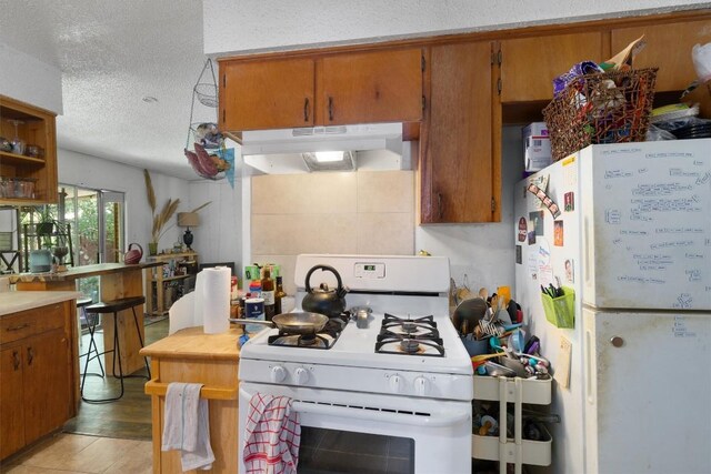 1905 Chestnut Ave, Austin, TX 78722 - kitchen featuring white appliances, under cabinet range hood, a textured ceiling, brown cabinets, and light countertops