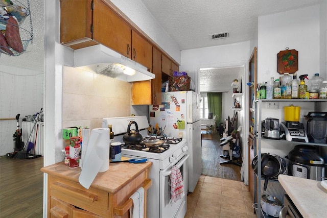 1905 Chestnut Ave, Austin, TX 78722 - kitchen featuring white range with gas stovetop, under cabinet range hood, light countertops, a textured ceiling, and brown cabinetry