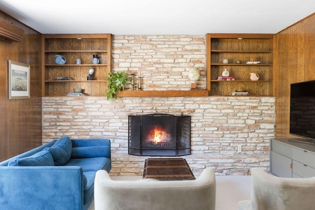 living area featuring a stone fireplace, wood walls, and built in shelves