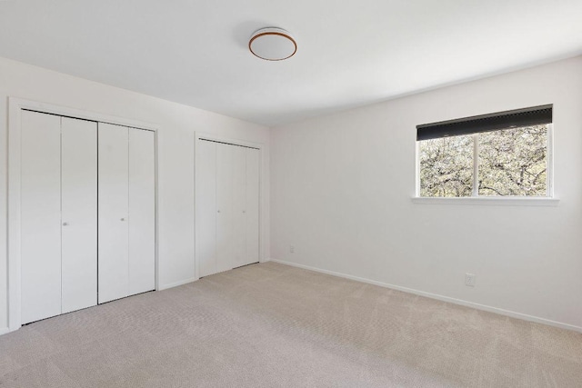 unfurnished bedroom featuring two closets, carpet floors, and baseboards