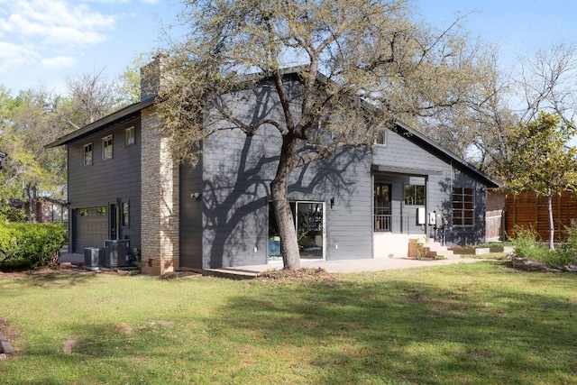 back of property with a lawn, a chimney, central AC, and an attached garage