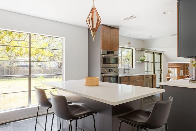 kitchen with brown cabinets, visible vents, a kitchen breakfast bar, and a sink