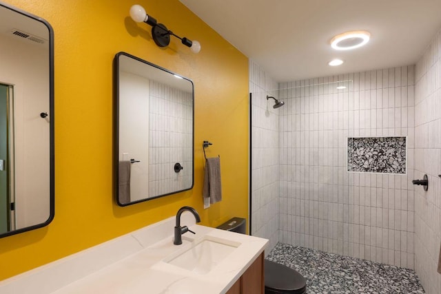 bathroom featuring visible vents, toilet, tiled shower, and vanity