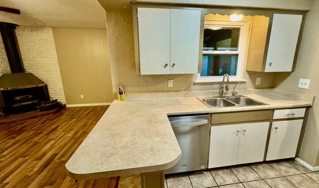 kitchen with light countertops, a sink, a wood stove, and stainless steel dishwasher