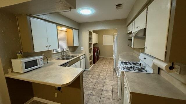 kitchen featuring visible vents, a peninsula, white appliances, a sink, and washer and dryer