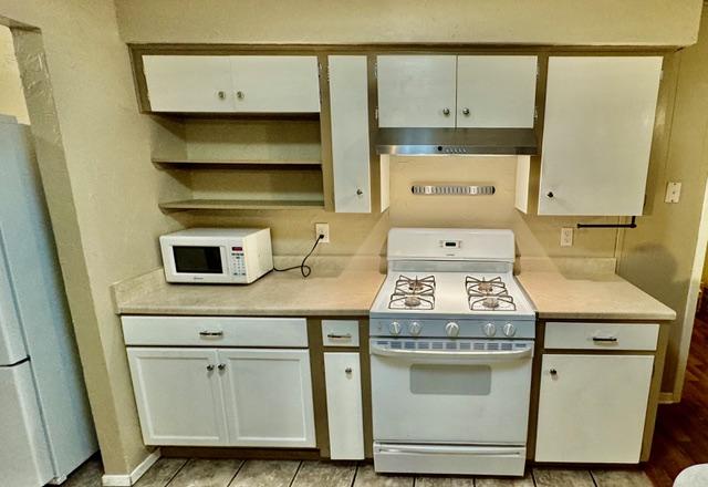 kitchen with white cabinetry, light countertops, open shelves, white appliances, and under cabinet range hood