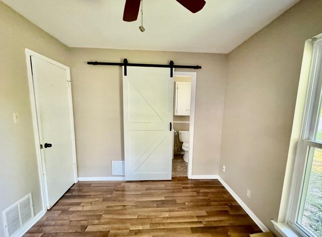 unfurnished bedroom with visible vents, baseboards, wood finished floors, a barn door, and ensuite bath