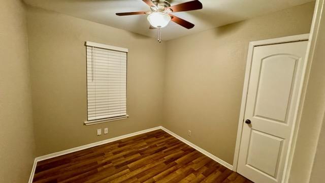 spare room featuring a ceiling fan, baseboards, and dark wood finished floors