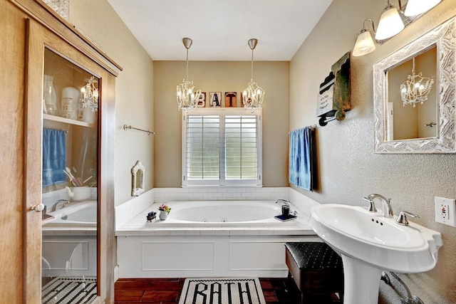 bathroom with a whirlpool tub, a textured wall, and an inviting chandelier