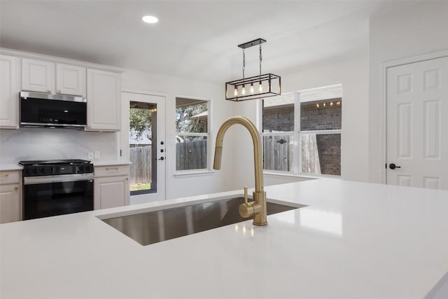 471 Bayou Bend Dr, Buda, TX 78610 - kitchen with stainless steel microwave, range with gas stovetop, a sink, light countertops, and hanging light fixtures