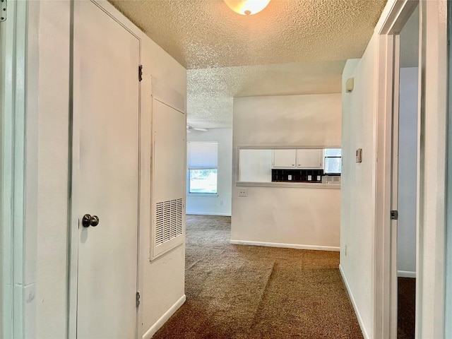 hall featuring baseboards, carpet, and a textured ceiling