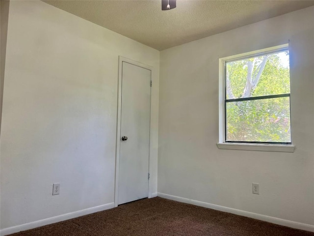 unfurnished room featuring dark carpet, baseboards, and a textured ceiling