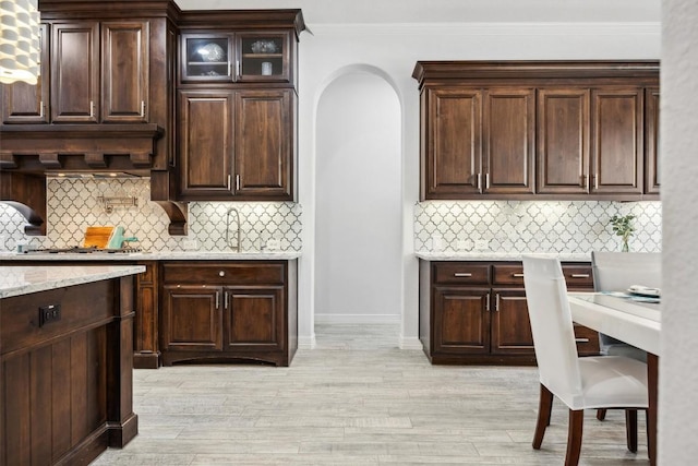 3801 Panther Hall, Leander, TX 78641 - kitchen featuring tasteful backsplash, dark brown cabinets, light wood finished floors, light stone countertops, and crown molding