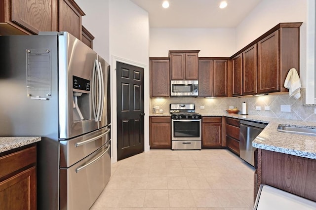 1909 Bobbywoods Ln, Manchaca, TX 78652 - kitchen featuring light stone countertops, dark brown cabinetry, stainless steel appliances, decorative backsplash, and light tile patterned floors