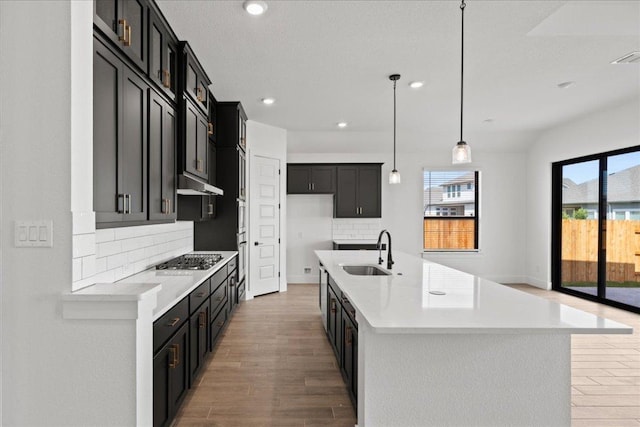 18716 Hopper Ln, Austin, TX 78738 - kitchen with light wood-style flooring, a sink, light countertops, stainless steel gas stovetop, and decorative backsplash