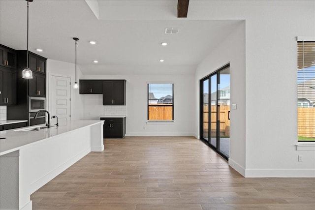 18716 Hopper Ln, Austin, TX 78738 - kitchen featuring stainless steel microwave, a sink, light wood-type flooring, visible vents, and dark cabinetry