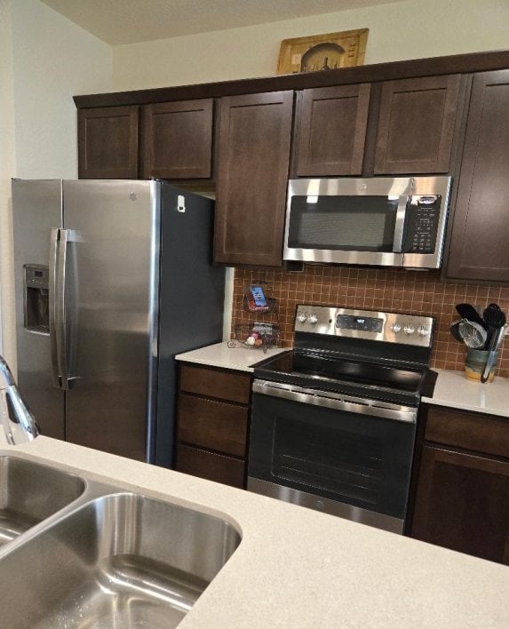 1717 Roseburg Dr, Austin, TX 78754 - kitchen with light countertops, stainless steel appliances, dark brown cabinetry, and decorative backsplash